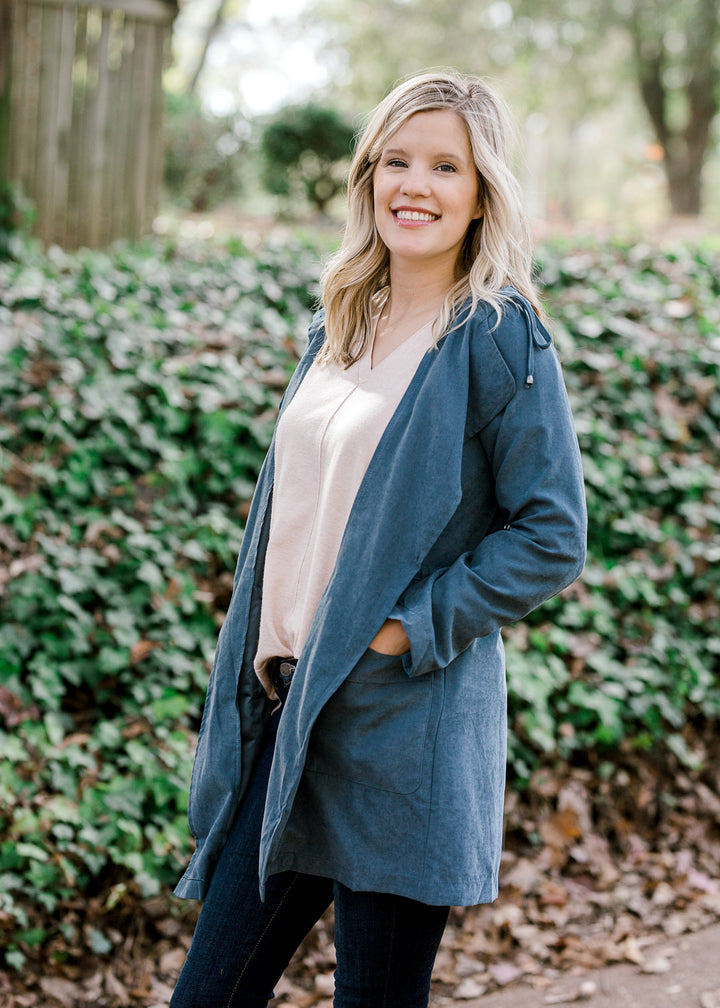 Blonde model wearing a slate blue jacket with a sand top and jeans.