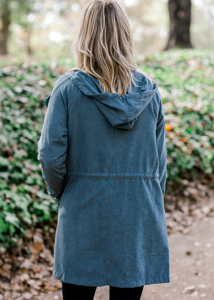 Back view of Blonde model wearing a slate blue jacket with a hood and tie at waist.