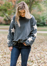Blonde model wearing slate blue sweater with cream star detail on sleeve.