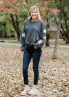 Blonde model wearing slate blue sweater with cream star detail on sleeve with jeans and booties.