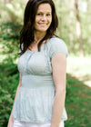 Brunette model wearing pale blue top with smocked waist.