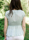 Back view of Brunette model wearing pale blue top with smocked waist.