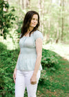 Brunette model wearing pale blue top with smocked waist and white jeans.