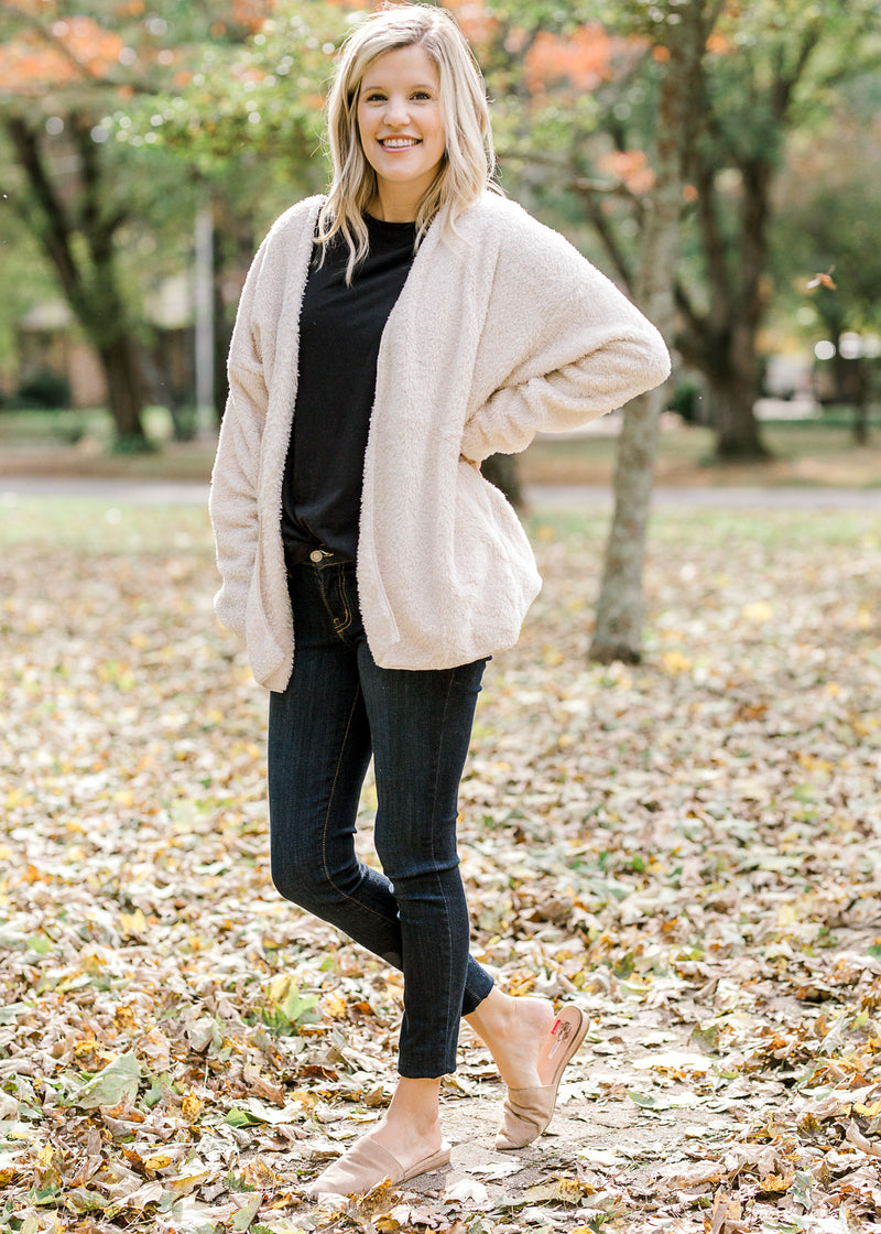 Blonde model is soft cream cardigan, jeans and slides.