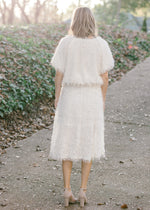 Back view of Blonde model wearing faux feather ivory top and skirt.