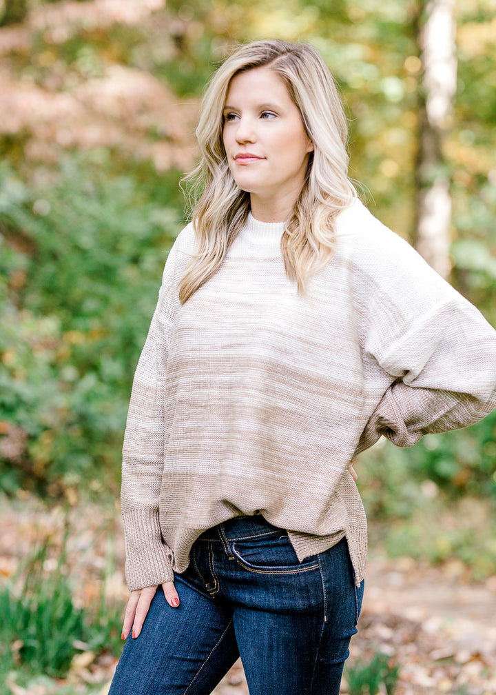 Blonde model wearing a cream to taupe transition sweater. 