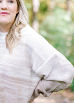 Close up view of Blonde model wearing a cream to taupe transition sweater. 