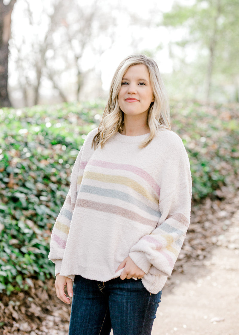 Blonde model wearing cream sweater with stripes with jeans.