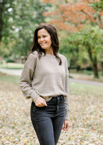 Brunette model wearing taupe sweater with gold shimmer detail and jeans.