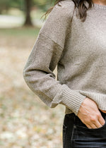 Close up view of sleeve on Brunette model wearing taupe sweater with gold shimmer detail.