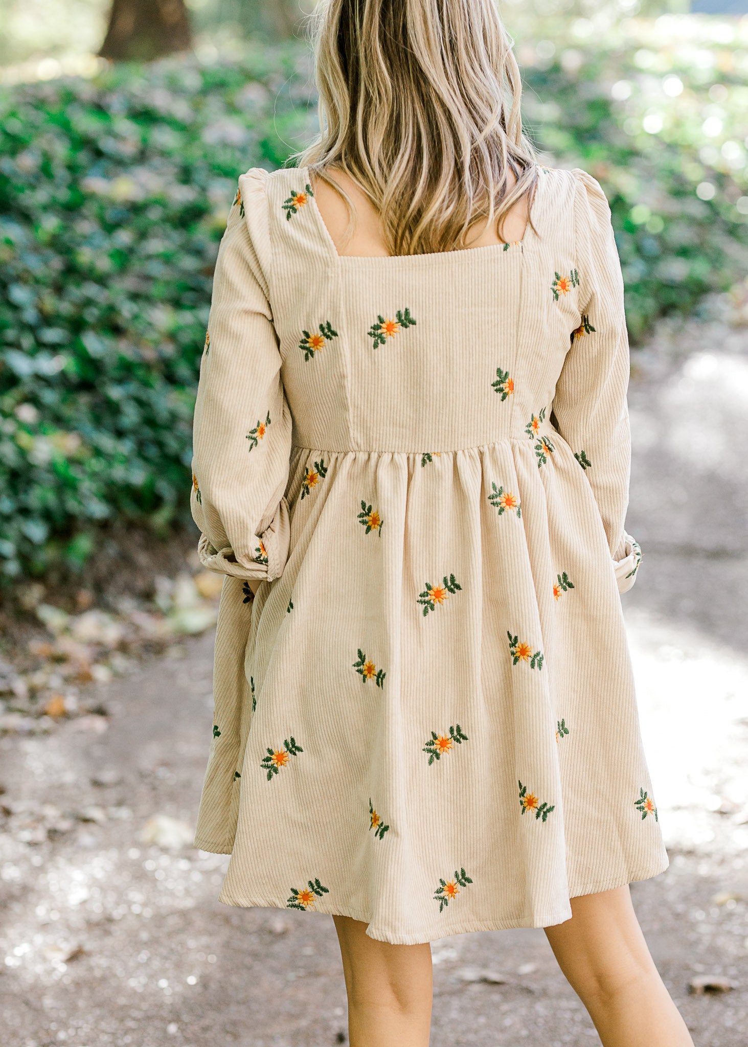 Back view of Blonde model wearing cream corduroy dress with sunflower embroidery.