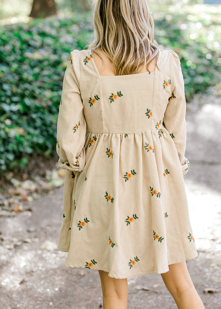 Back view of Blonde model wearing cream corduroy dress with sunflower embroidery.