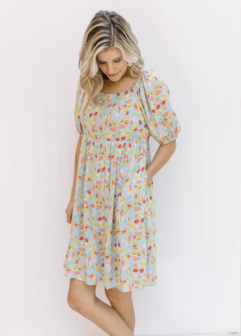 Model wearing an above the knee light blue babydoll dress with a bright floral design. 