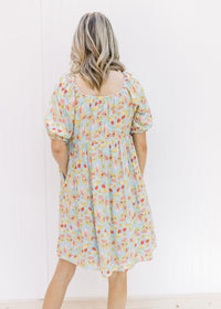 Back view of Model wearing an above the knee light blue babydoll dress with a bright floral design. 