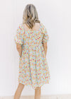 Back view of Model wearing an above the knee light blue babydoll dress with a bright floral design. 