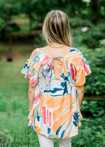 Back view of Blonde model wearing a cream top with a watercolor pattern.