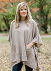 Blonde model wearing taupe poncho with front pockets.