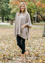 Blonde model wearing taupe poncho with black jeans and heeled mules.