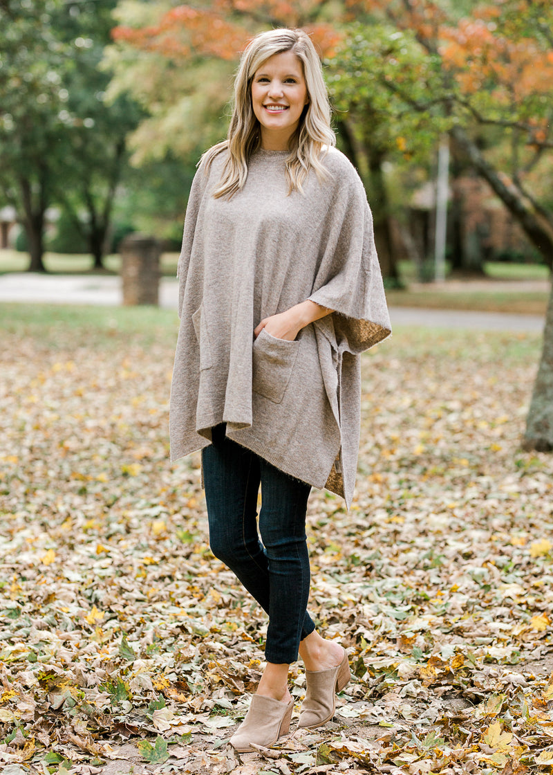 Blonde model wearing taupe poncho with black jeans and heeled mules.