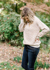 Blonde model wearing a taupe and cream zig zag sweater. 