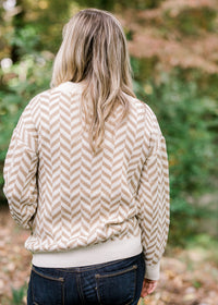 Back view of Blonde model wearing a taupe and cream zig zag sweater. 