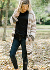 Blonde model wearing a cream, taupe and brown striped cardigan. 
