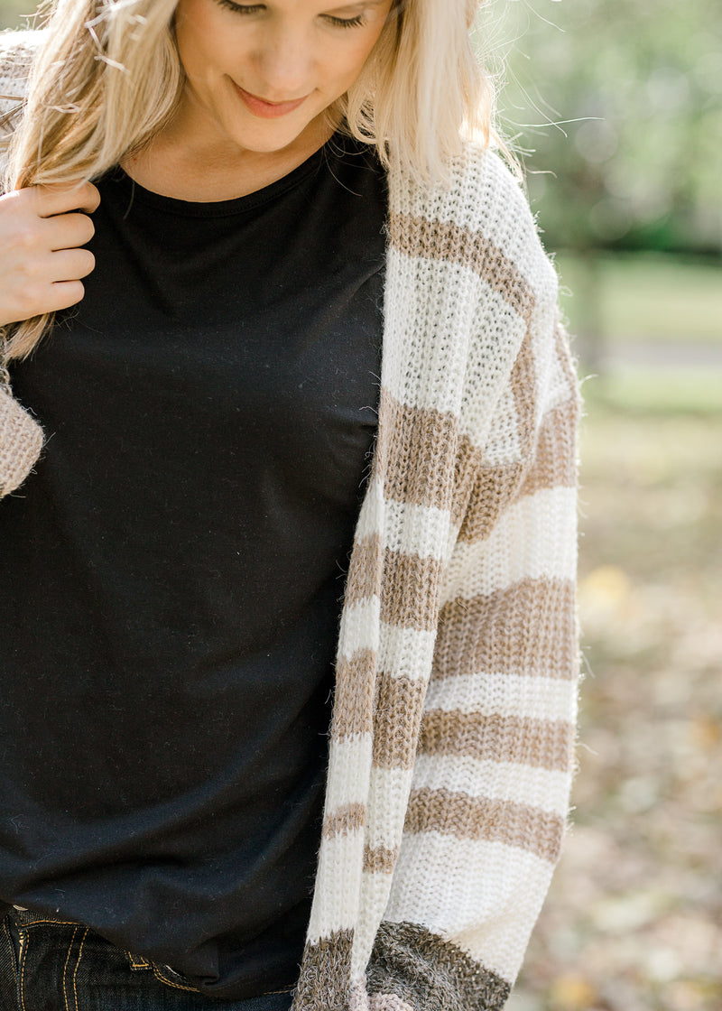 Blonde model wearing a cream, taupe and brown striped cardigan with a black top.