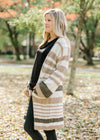 Side view of Blonde model wearing a cream, taupe and brown striped cardigan. 