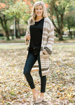 Blonde model wearing a cream, taupe and brown striped cardigan with black top, jeans and mules.