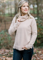 Blonde model wearing a taupe sweater with a cowl neck. 