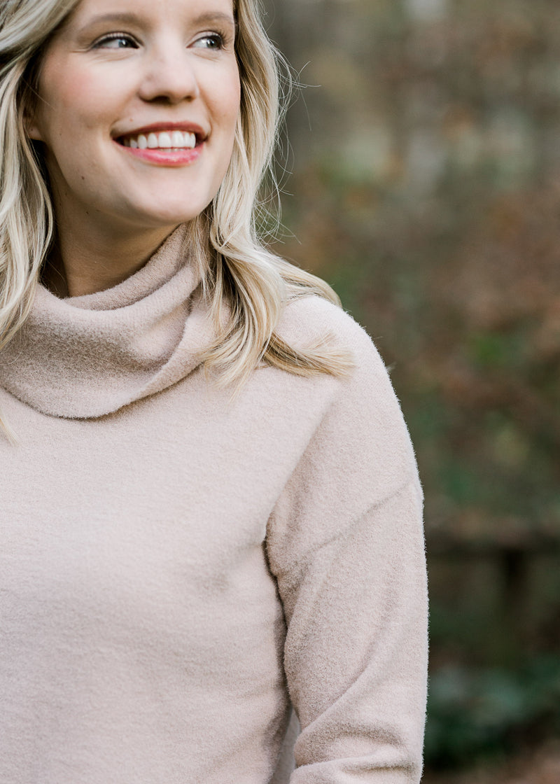 Close up view of Blonde model wearing a taupe sweater with a cowl neck. 