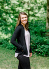 Brunette model wearing front zip athleisure jacket and black leggings.