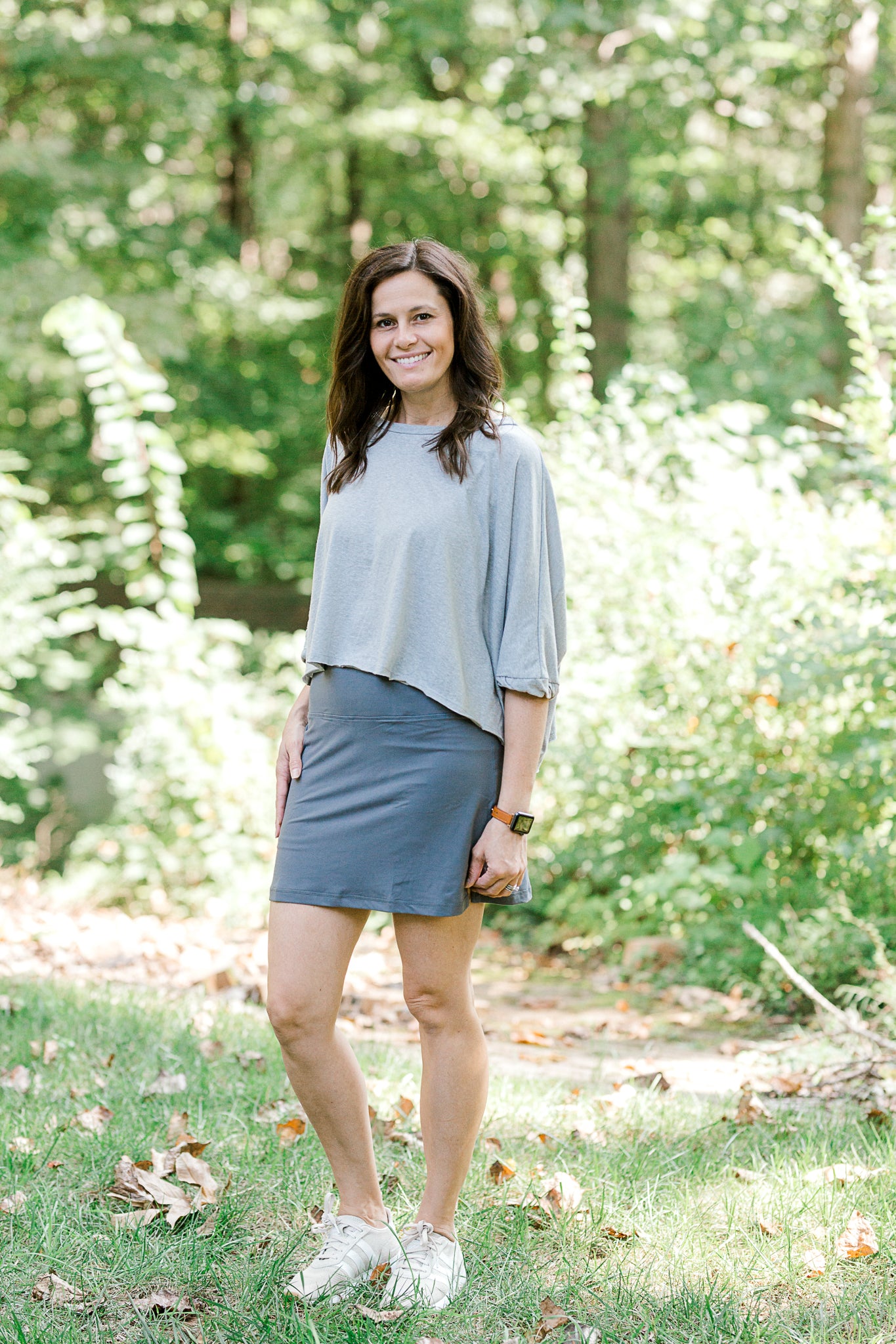 Brunette model wearing a gray tennis skirt and sneakers.