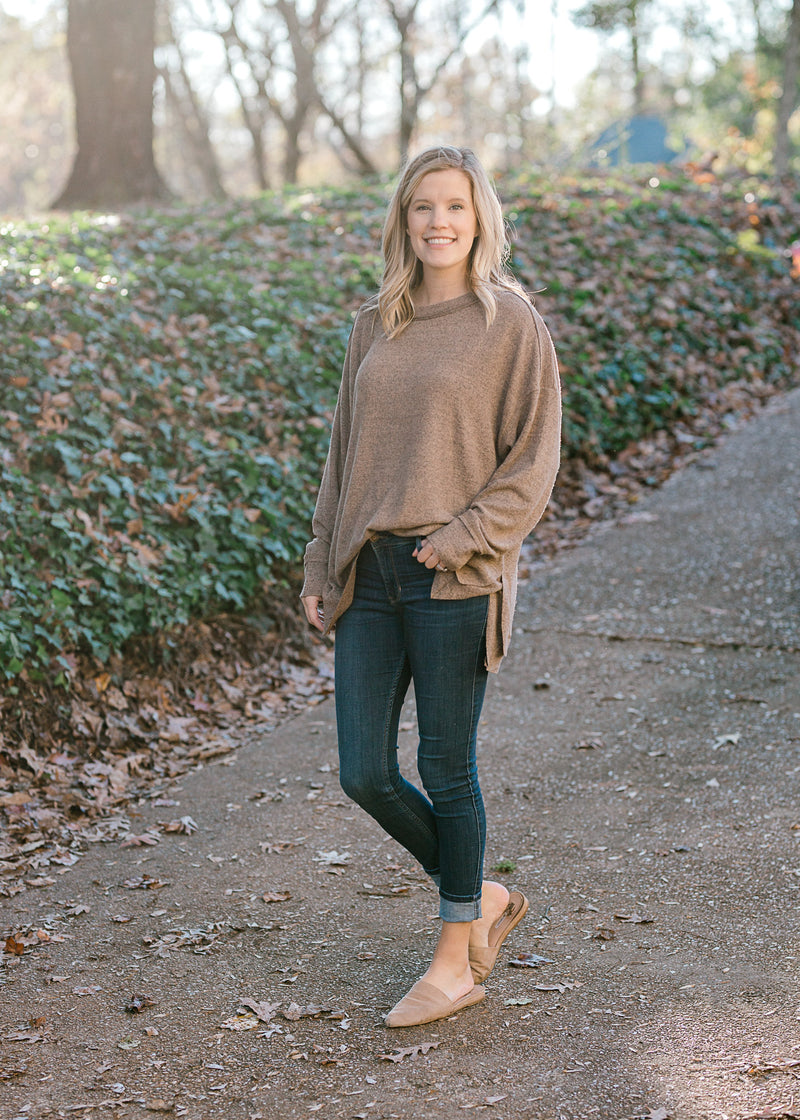 Blonde model wearing heathered light brown sweater with jeans and mules. 