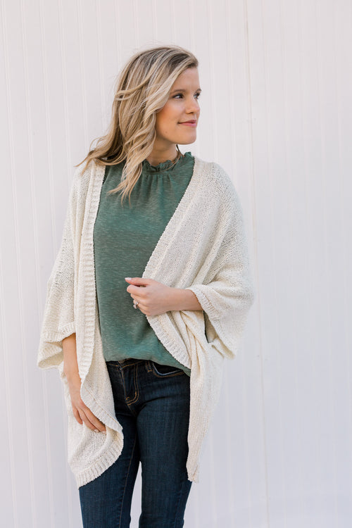 Blonde model wearing a cream cardigan with batwing sleeves. 