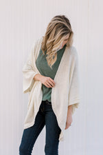 Blonde model wearing green top with a cream cardigan with batwing sleeves.