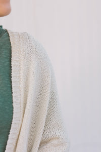 Close up view of Blonde model wearing a cream cardigan with batwing sleeves. 