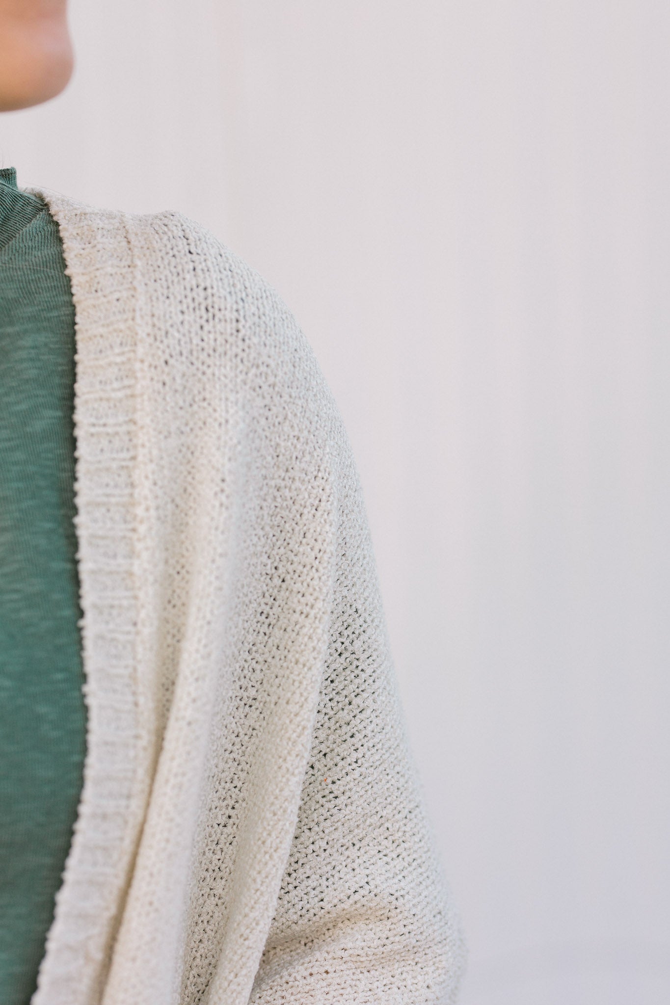 Close up view of Blonde model wearing a cream cardigan with batwing sleeves. 