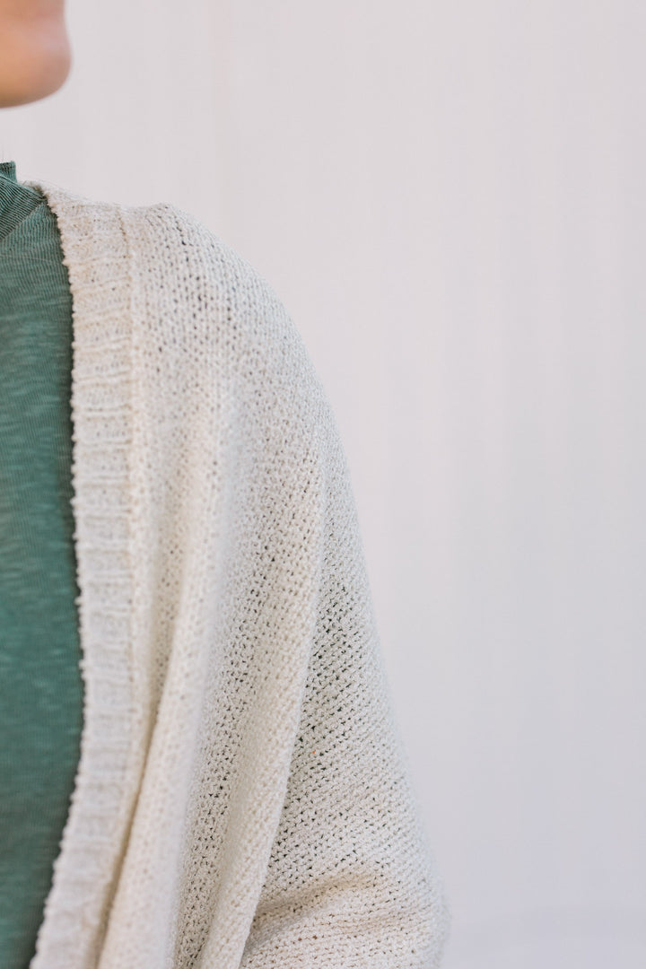 Close up view of Blonde model wearing a cream cardigan with batwing sleeves. 