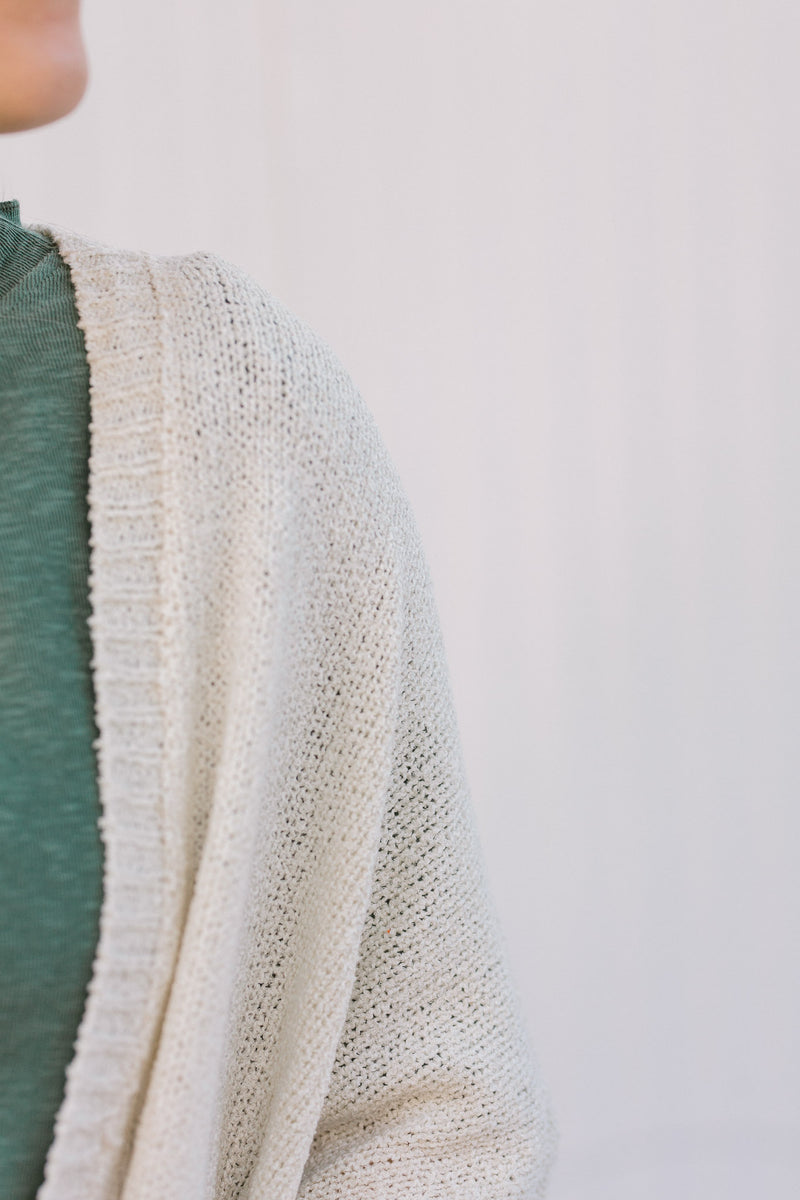 Close up view of Blonde model wearing a cream cardigan with batwing sleeves. 