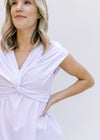 Model wearing a white v-neck blouse with a twisted bust and capped sleeves.