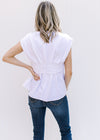 Back view of Model wearing a white v-neck blouse with a twisted bust and capped sleeves.