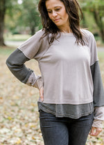 Brunette model wearing ash and charcoal two toned top with jeans.