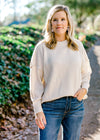 Blonde model wearing a cream colored sweater with jeans.