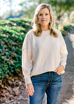 Blonde model wearing a cream colored sweater with jeans.