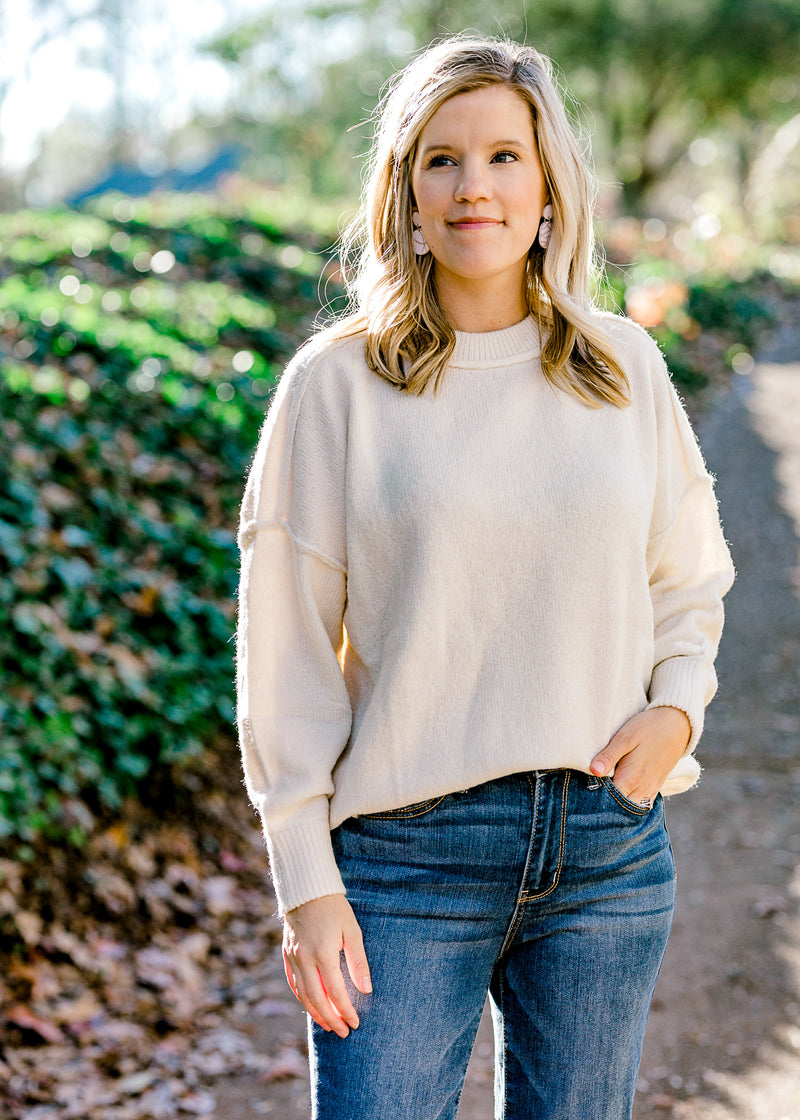 Blonde model wearing a cream colored sweater with jeans.