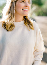 Close up view of Blonde model wearing a cream colored sweater with exposed hem.