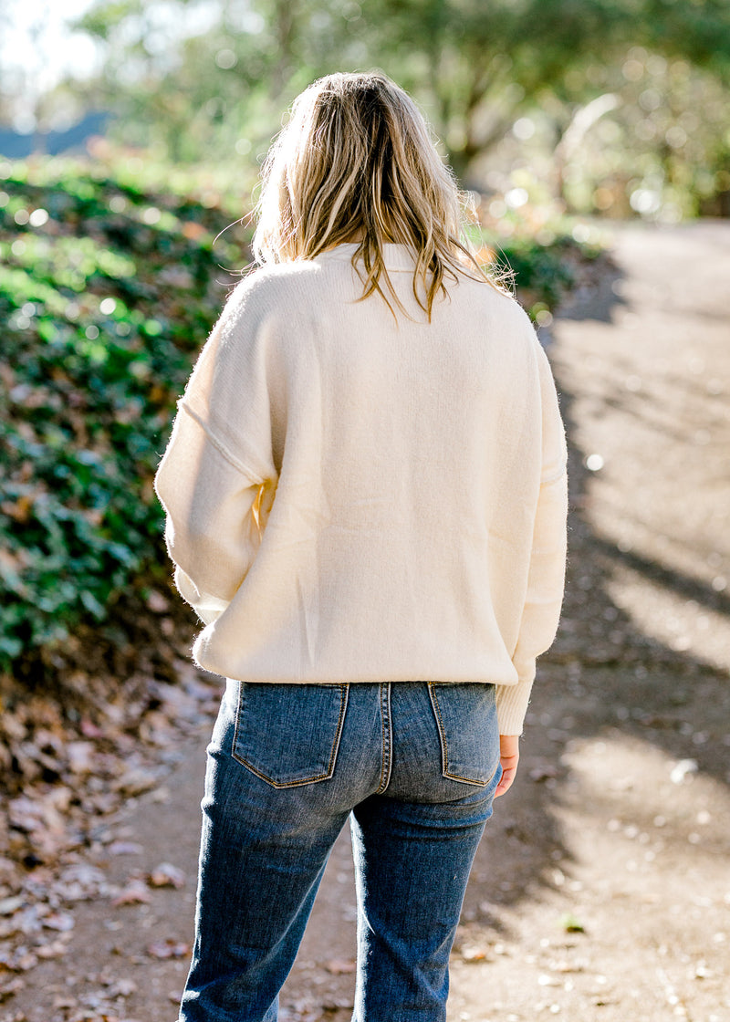 Back view of Blonde model wearing a cream colored sweater with jeans.