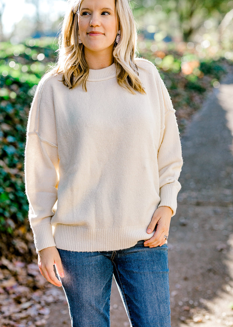 Blonde model wearing a cream colored sweater with exposed hem.
