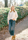 Blonde model wearing a cream colored sweater with jeans and booties.
